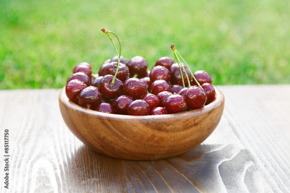 Wooden plate full with ripe red cherries in sun flare Wooden plate full with ripe red cherries in sun flare
