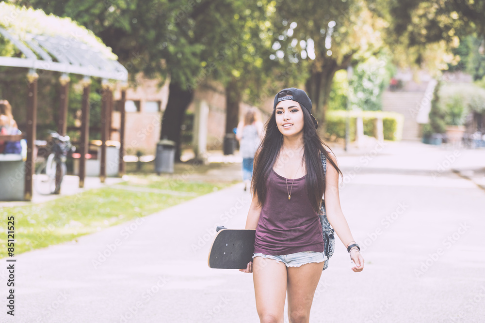 Beautiful girl walking at park holding a skateboard.