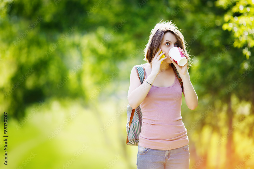 Woman wearing casual clothes talking on phone and drinking beverage Woman wearing casual clothes talking on phone and drinking beverage