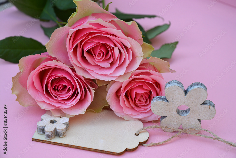 pink painted wooden background with bunch of pink roses and wooden label decorated