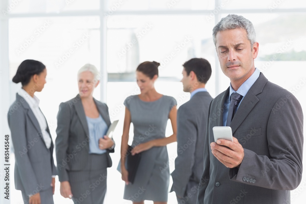 Businessman using mobile phone with colleagues behind