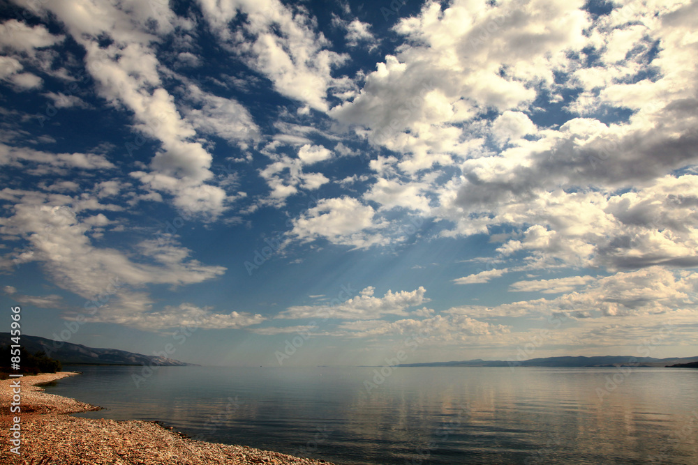 Fototapeta premium Sunshine make the way through clouds on water, Baikal lake
