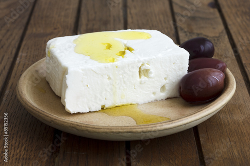 Greek feta cheese, oil, kalamata olives on rustic plate board.