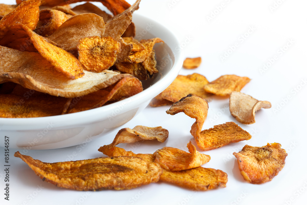 White bowl of fried carrot and parsnip chips. On white.