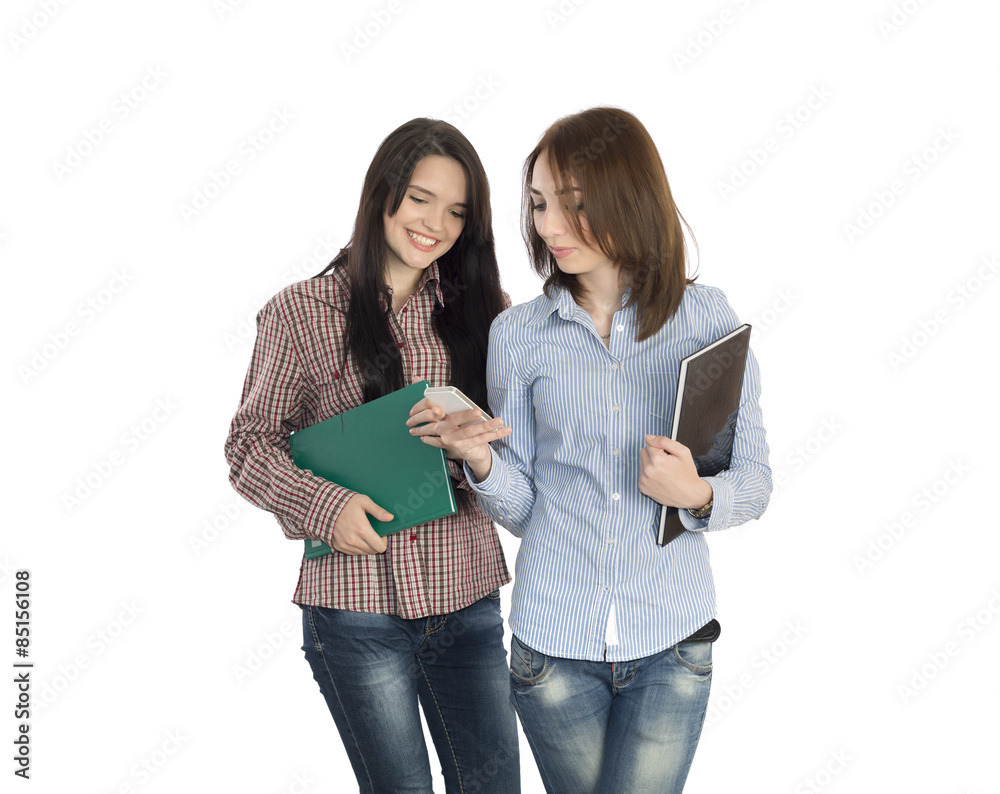 Stockfoto Female student shows funny things on phone screen to her friend.  Two young women student style jeans dress keeping notepads and mobile phone  and laughing on white background | Adobe Stock