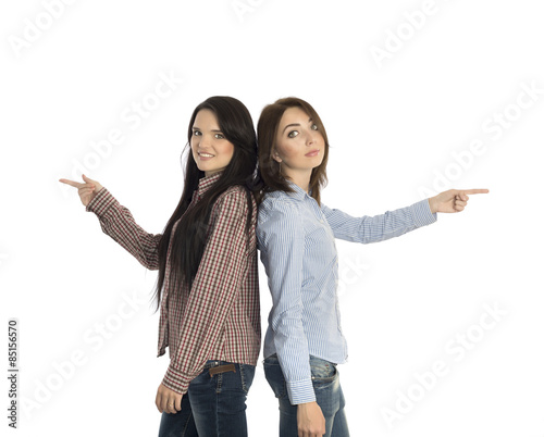 Two smiling girls pointing to opposite directions.
Two young women stay back to back and pointing hands into opposite directions on white background casually dressed jeans style