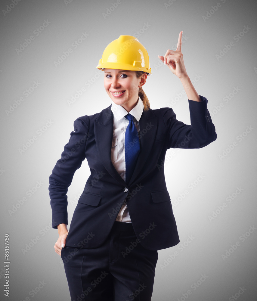Young businesswoman with hard hat against gradient 