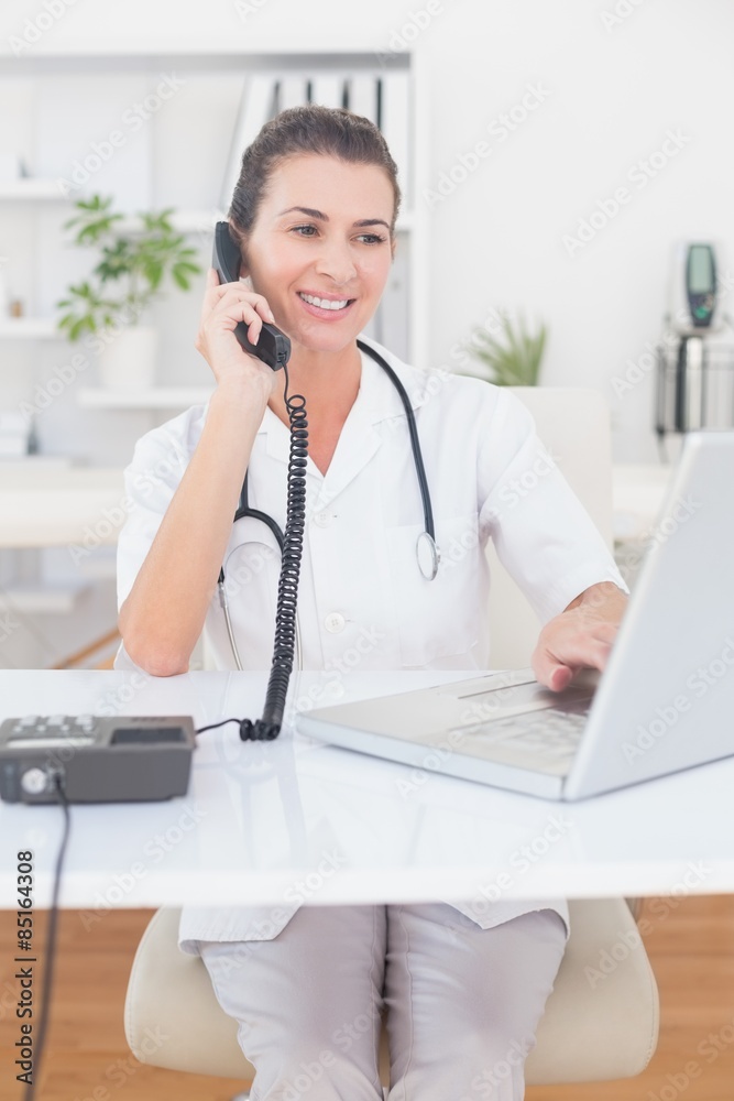 Doctor doing phone call while she using computer Doctor doing phone call while she using computer