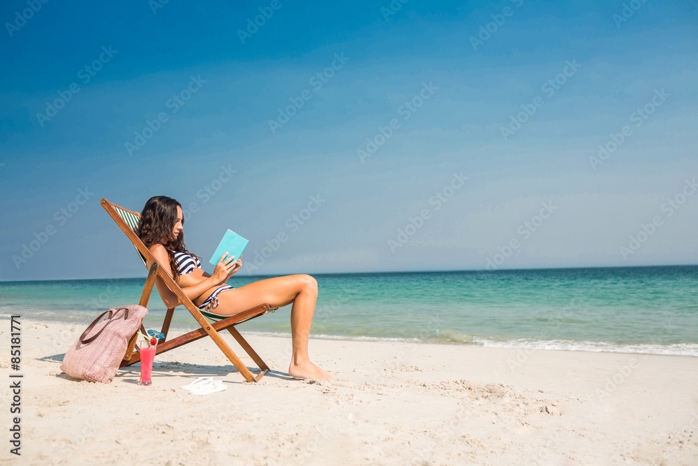 Pretty brunette reading a book on deck chair