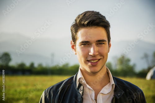 Handsome smiling young man at countryside, in front of field or
