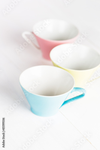 Three pastel colored china coffee cups on white wood