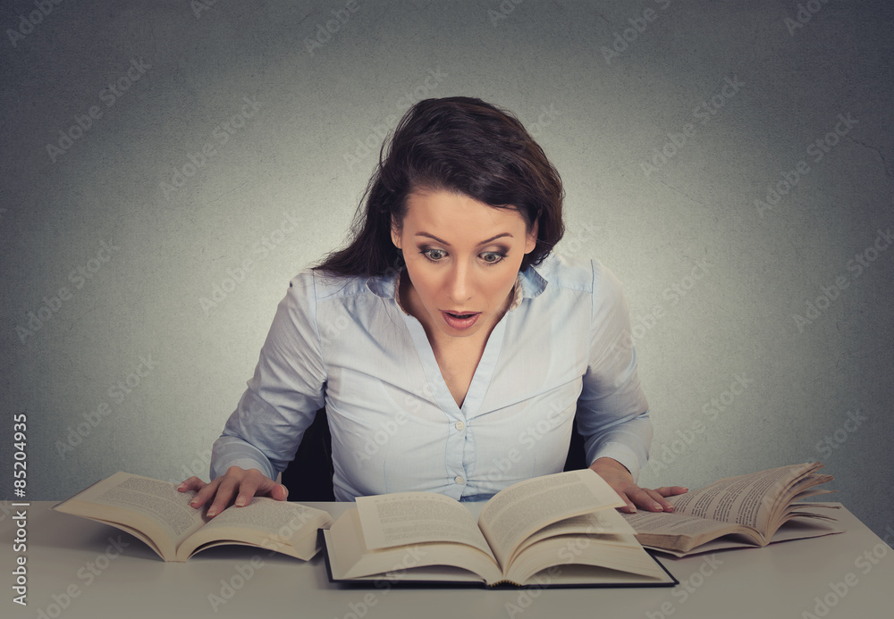 shocked woman sitting at desk with many opened books reading shocked woman sitting at desk with many opened books reading