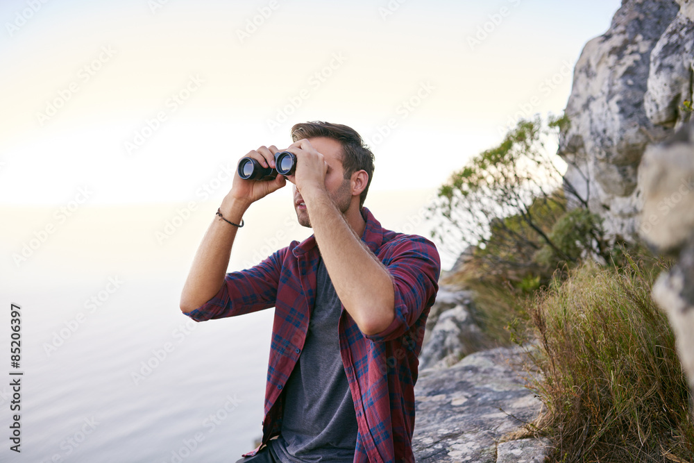 Young man on a rocky mountainside with binoculars Young man on a rocky mountainside with binoculars