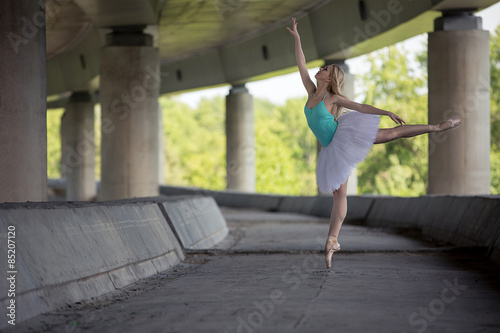 Graceful ballerina doing dance exercises on a concrete bridge 