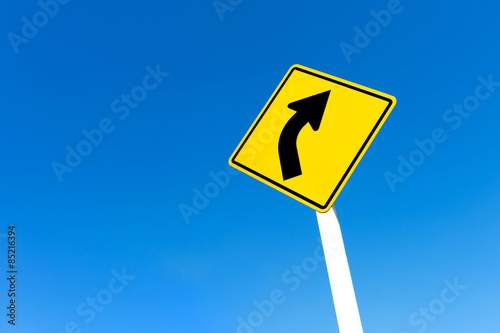 Yellow traffic right curve sign on blue sky background.