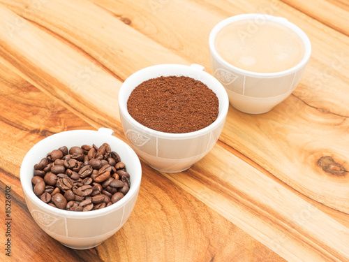 drei Tassen mit Kaffee, Kaffeebohnen und Kaffeepulver auf Holzti