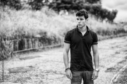 Young man in jeans and black t-shirt walking along rural road