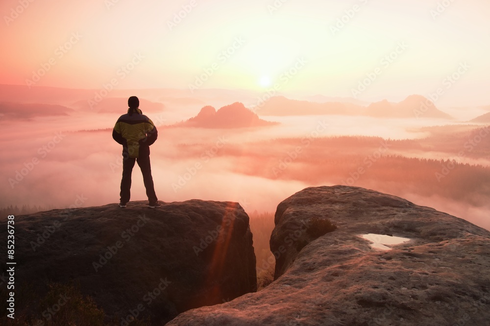 Moment of loneliness. Man on the rock empires  and watch over the misty and foggy morning valley to Sun