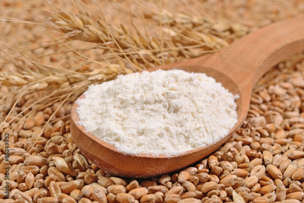 White flour in a wooden spoon and ears of wheat on a wheat grain White flour in a wooden spoon and ears of wheat on a wheat grain