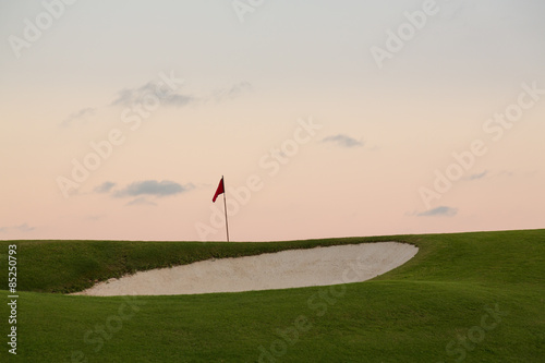 Sand bunker in front of golf green and flag