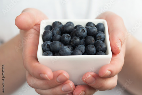 Hands holding white bowl full of blueberries
