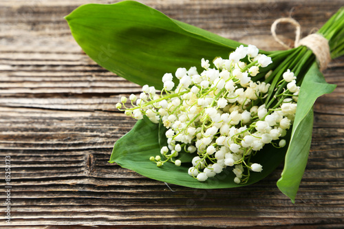 Fotografija Lily of the Valley with leaves on brown wooden background