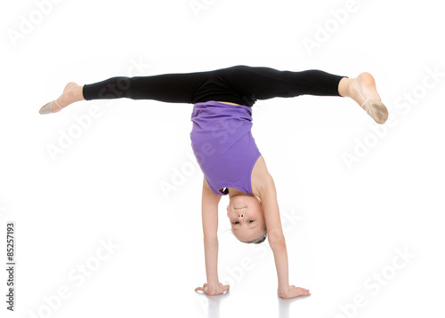 The girl athlete is on his hands and doing the splits