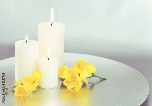 Candles and yellow Freesia blossoms with silver background. 