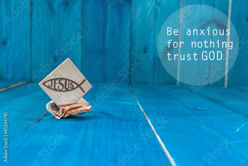 Inspirational motivating quote saying that God has everything in control. Christian fish symbol carved in wood and blue vintage wooden background