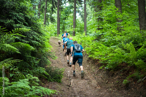 four men running hard up the hill in the forest with fern