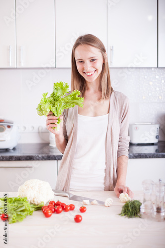 smiling young woman standing in kitchen , holding bright green s