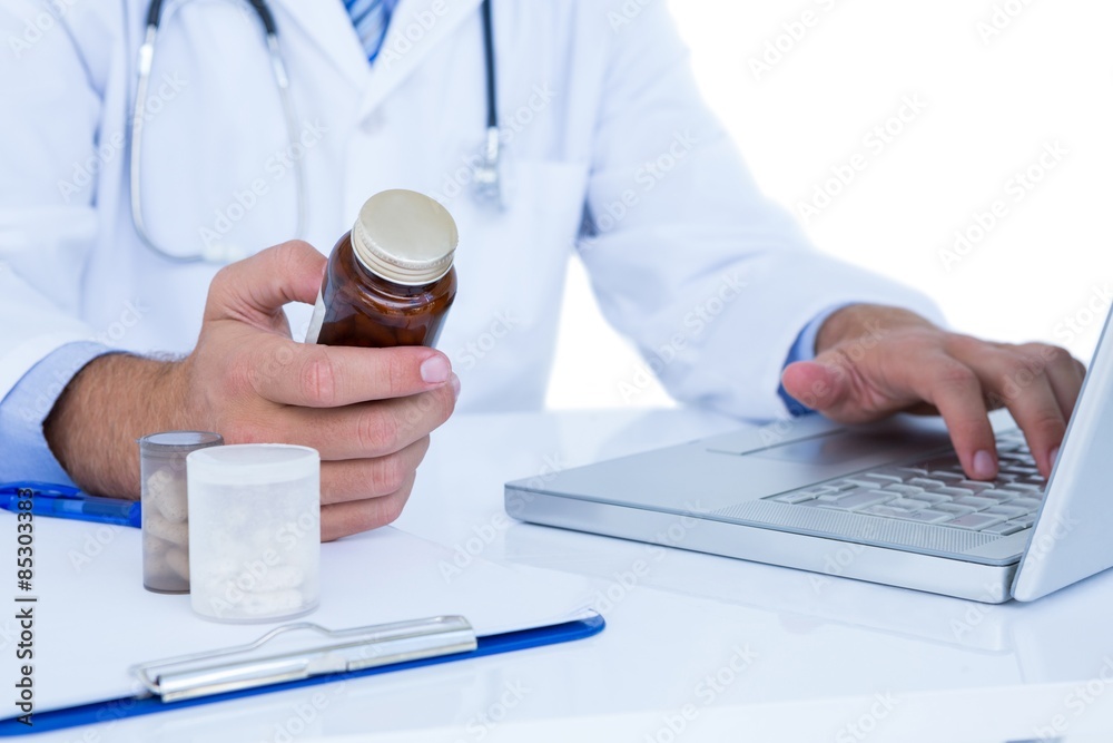 A doctor holding a medecine while typing on a laptop