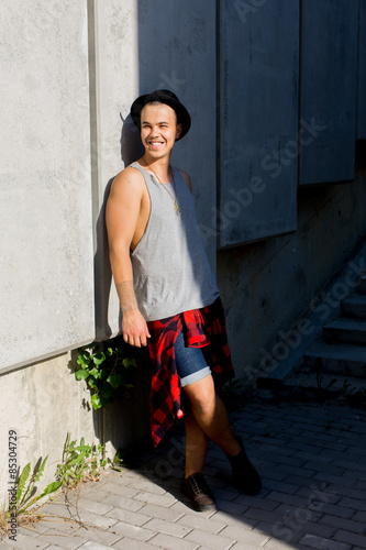 cool young and handsome caucasian brunette hipster skater guy wearing a hat posing smiling and having fun outside during amazing summer day in the city with
