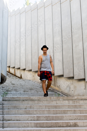 cool young and handsome caucasian brunette hipster skater guy wearing a hat posing smiling and having fun outside during amazing summer day in the city with