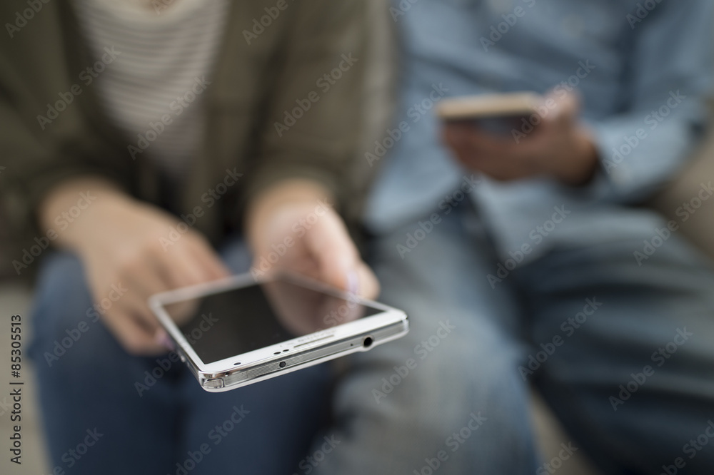 The couple are looking at a smart phone sitting on the sofa The couple are looking at a smart phone sitting on the sofa