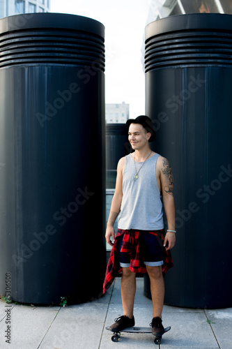 cool young and handsome caucasian brunette hipster skater guy wearing a hat posing smiling and having fun outside while skating with his skateboard during amazing summer day in the city