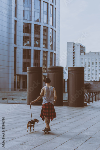 cool young and handsome caucasian brunette hipster skater guy wearing a hat posing smiling and having fun outside while skating with his skateboard summer day in the city with beagle pupppy dog