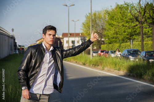 Handsome young man, hitchhiker waiting on roadside