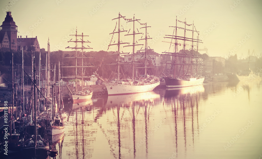 Retro toned photo of sailing ships at sunrise, Szczecin, Poland.