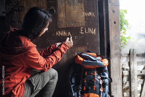 Austria, Altenmarkt-Zauchensee, young female hiker carving her name in wooden door of Alpine Cabin photo