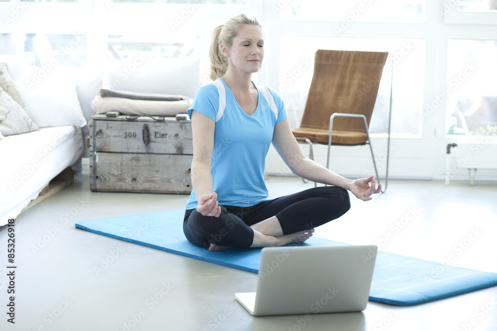 Woman with laptop practicing yoga on gym mat in living room