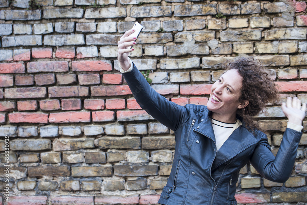 Smiling woman taking selfie in front of brick wall