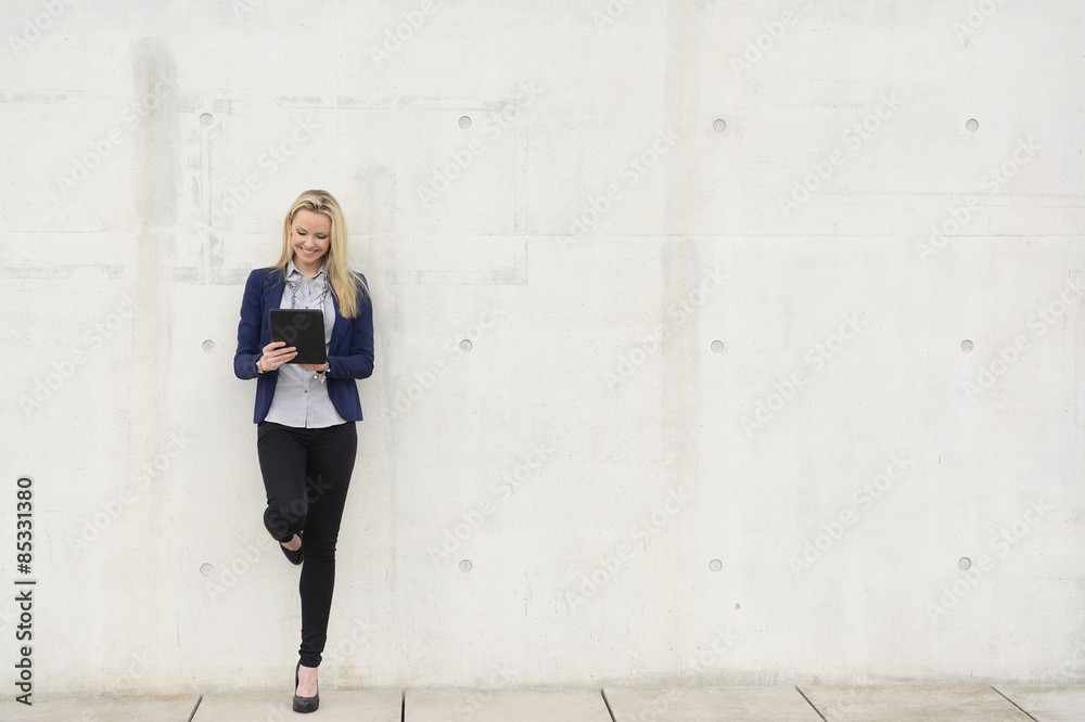 Smiling businesswoman with digital tablet leaning on concrete wall Smiling businesswoman with digital tablet leaning on concrete wall