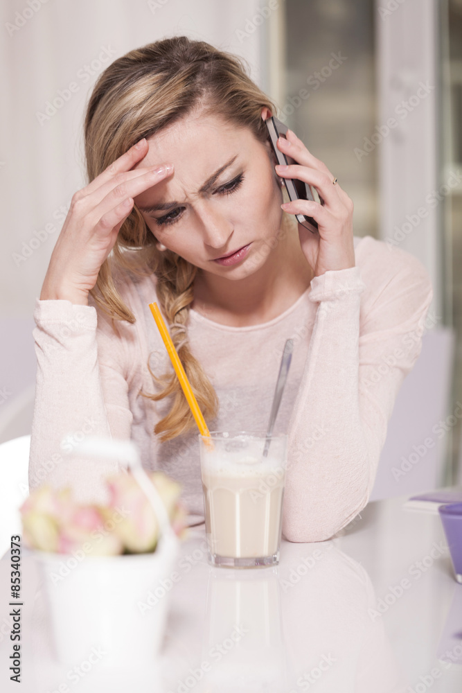 Unhappy blond woman sitting in a coffee shop telephoning with smartphone Unhappy blond woman sitting in a coffee shop telephoning with smartphone