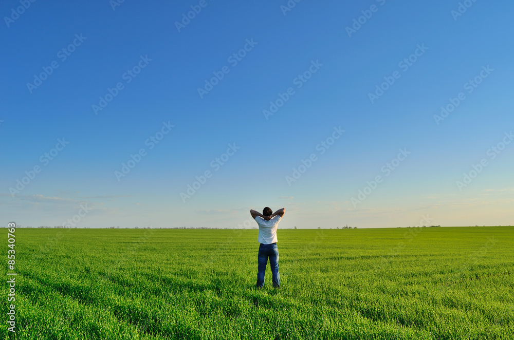 Young man on the summer green field under clear skies Young man on the summer green field under clear skies