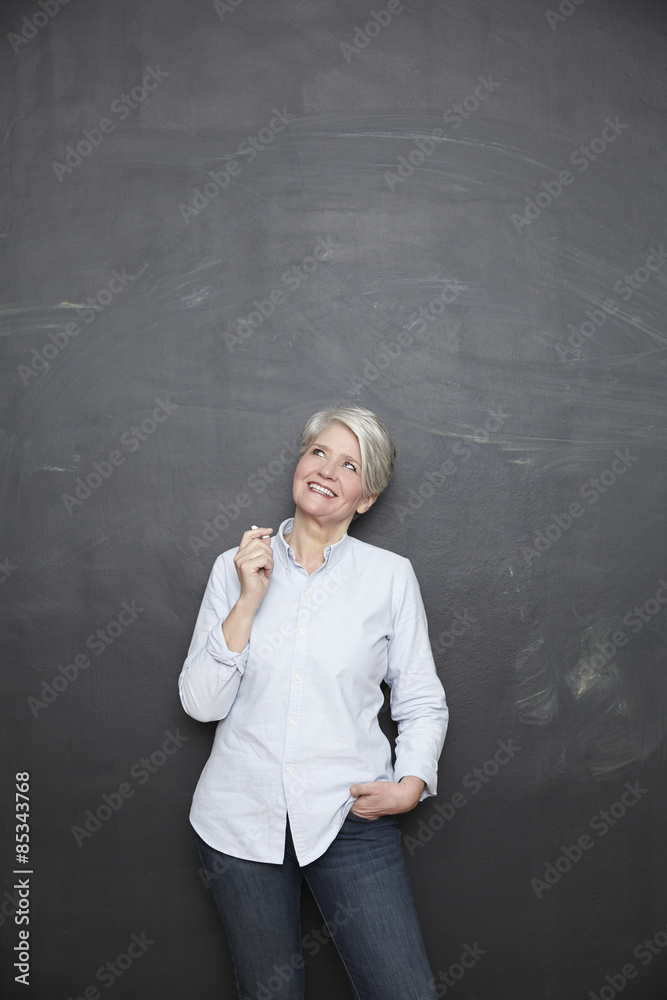 Smiling mature teacher standing at blackboard looking up Smiling mature teacher standing at blackboard looking up