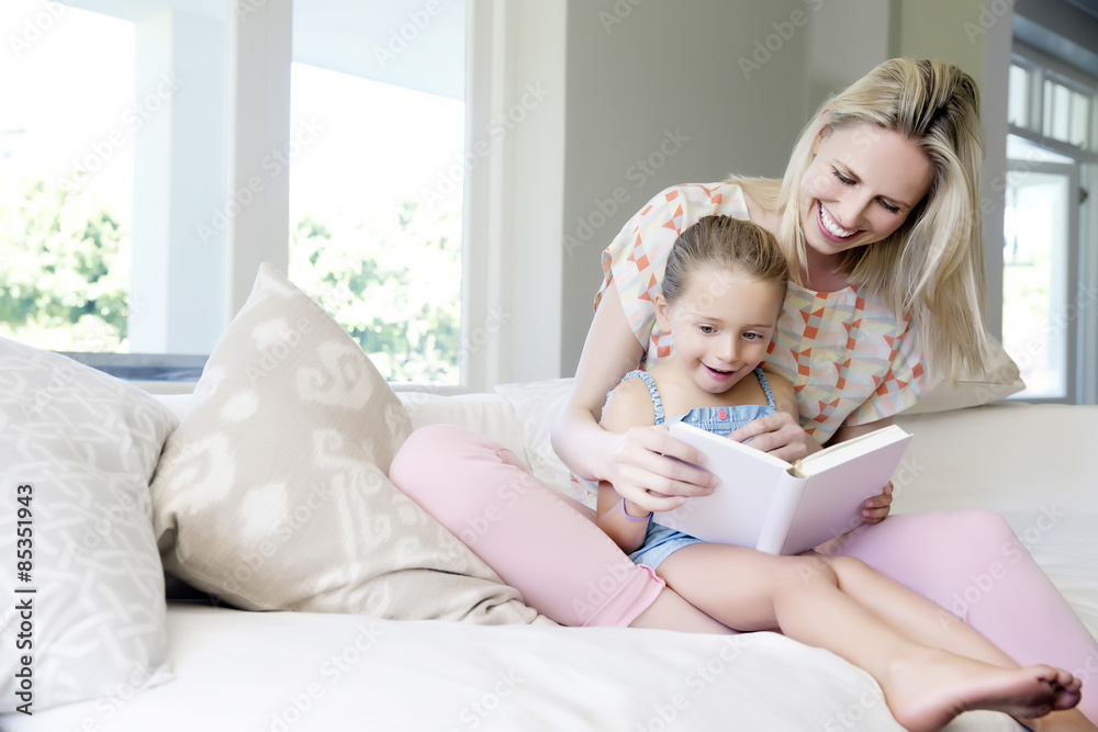 Mother and daughter sitting on sofa, reading book Mother and daughter sitting on sofa, reading book