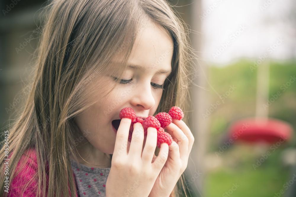 Girl eating raspberries from her fingers