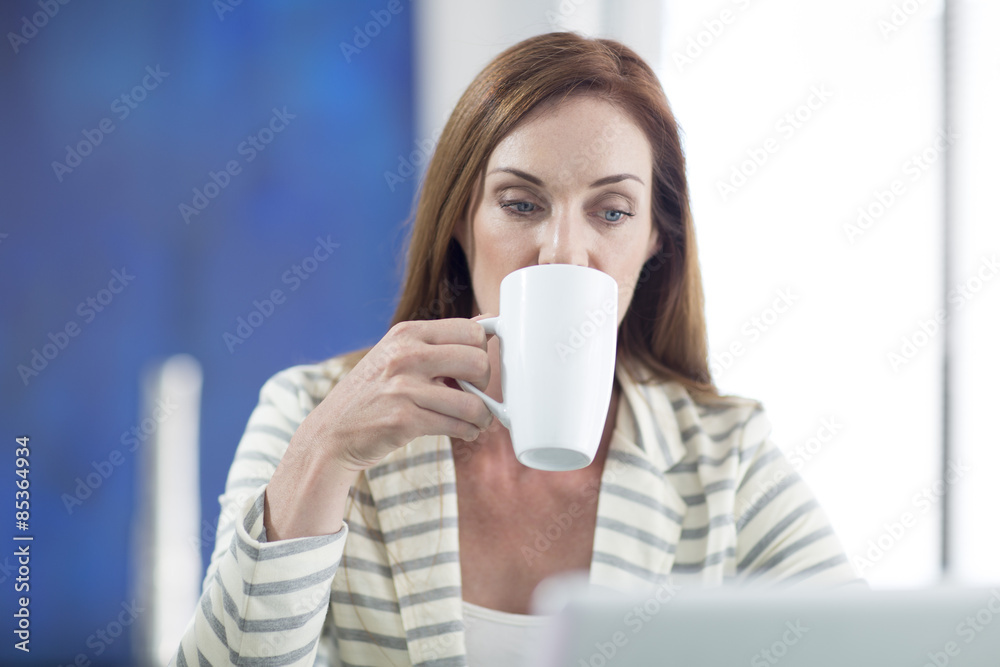 Businesswoman in office drinking coffee and working on laptop Businesswoman in office drinking coffee and working on laptop