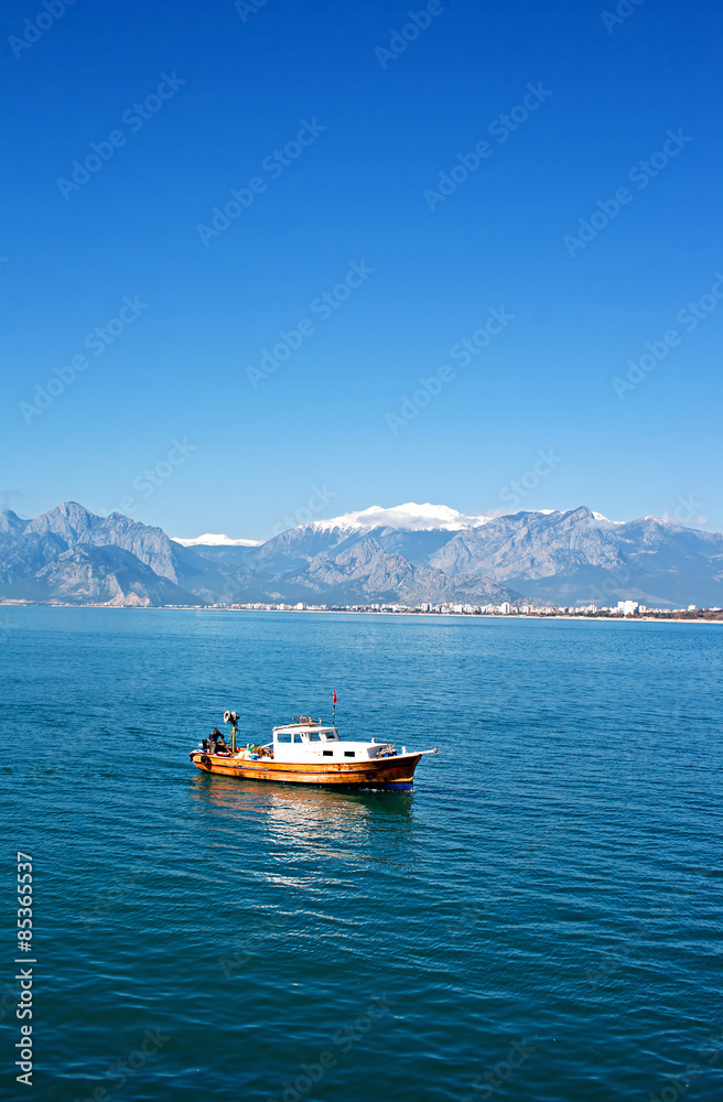 Small fishing boat with snow covered mountains in Antalya Turkey Small fishing boat with snow covered mountains in Antalya Turkey
